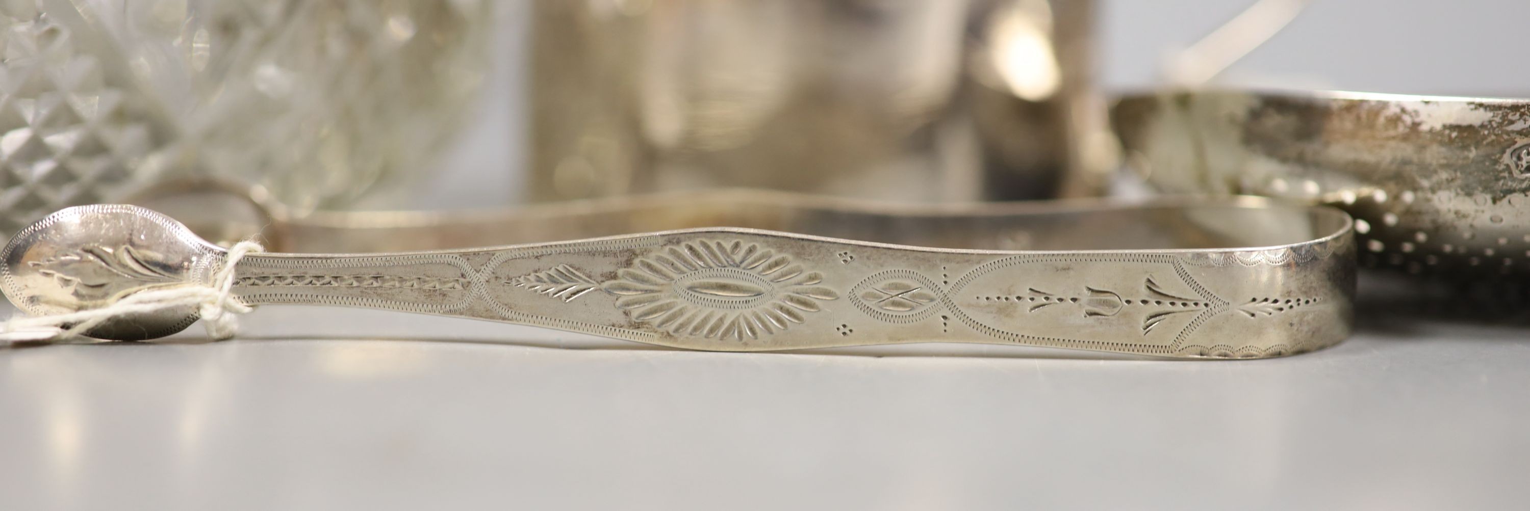 A small selection of decorative silver items to include a Georgian pierced strainer, a mustard pot, pair of sugar tongs and a mounted glass jar (lacking cover).